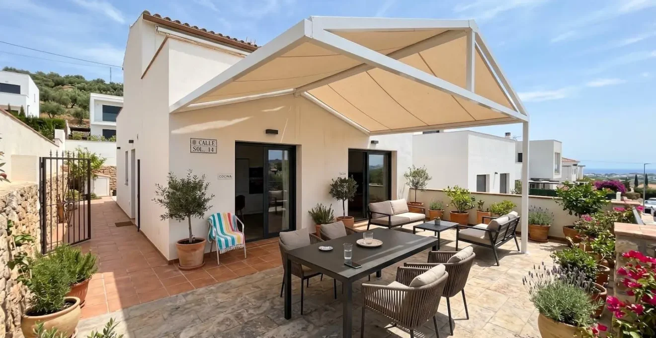 Vista amplia de un patio residencial contemporáneo español con toldo dos aguas instalado, muebles de exterior bajo sombra y luz natural mediterránea