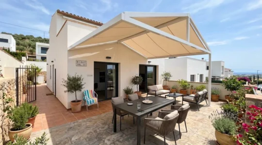 Vista amplia de un patio residencial contemporáneo español con toldo dos aguas instalado, muebles de exterior bajo sombra y luz natural mediterránea